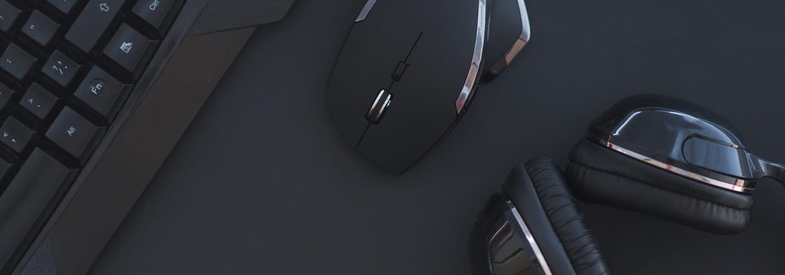 Black mouse, the keyboard, the headphones are isolated on a dark background, the top view. Flat lay gamer background. Workspace with a keyboard and mouse on a black background. Copyspace